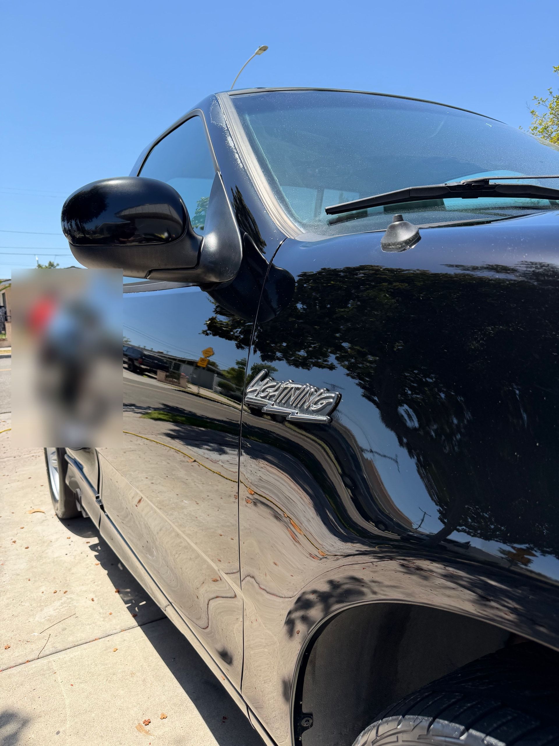 The same driver side after detailing, with deep black paint reflecting the street and a clean Lightning badge.