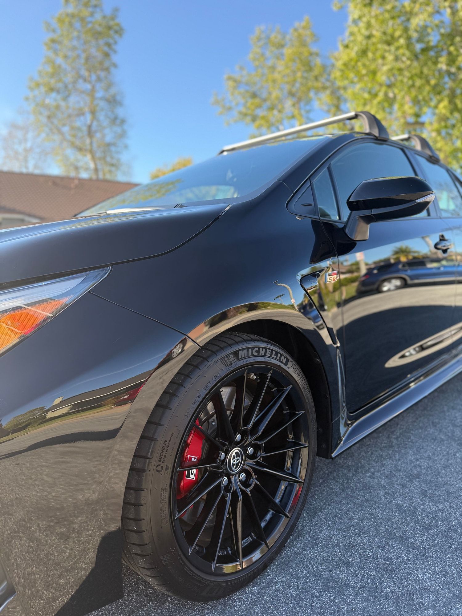 Mirror-gloss black door and fender of a Toyota GR Corolla reflecting the street